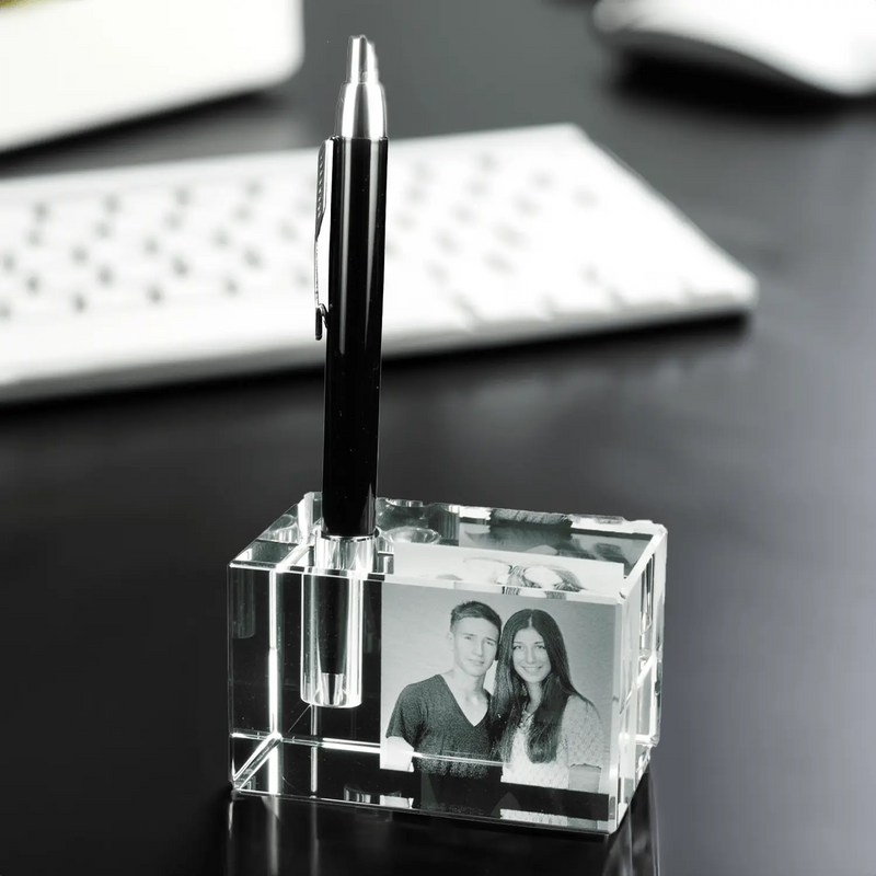 Der Engravy 2D-Stiftehalter mit Foto-Gravur ist ein eleganter Stiftehalter aus klarem Acryl für den Schreibtisch. Er ist mit einem schwarzen Stift und einem personalisierten Schwarzweißfoto eines lächelnden Paares auf einer dunklen Oberfläche mit einer weißen Tastatur versehen. Für eine zusätzliche persönliche Note können Sie ihn mit einer individuellen Gravur personalisieren.