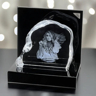 Die Engravy 3D-Glasgravur – The Rock zeigt eine Kristall-Fotoskulptur im Premium-Design auf schwarzem Untergrund, die ein Graustufenporträt einer Frau in einer gemusterten Bluse zeigt, die ihr langes Haar hält. Hergestellt aus Kristallglas mit verschwommenen weißen Lichtakzenten, unterstreicht es die exquisite Handwerkskunst.
