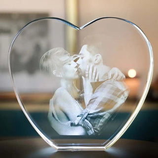 Das 3D-Glas-Herz von Engravy ist eine herzförmige Skulptur, die mit Lasertechnologie gefertigt wurde und einen schwarz-weißen Kuss eines Paares zeigt. Es ruht auf einer dunklen Oberfläche mit verschwommenem Hintergrund und wird für einen besonderen Reiz von einem LED-Leuchtsockel beleuchtet.
