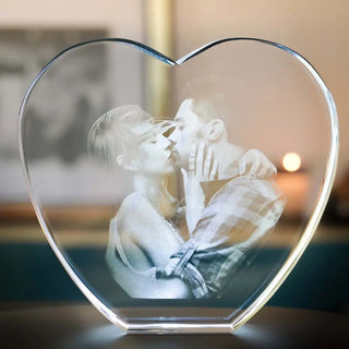 Das 3D-Glas-Herz von Engravy ist eine herzförmige Skulptur, die mit Lasertechnologie gefertigt wurde und einen schwarz-weißen Kuss eines Paares zeigt. Es ruht auf einer dunklen Oberfläche mit verschwommenem Hintergrund und wird für einen besonderen Reiz von einem LED-Leuchtsockel beleuchtet.