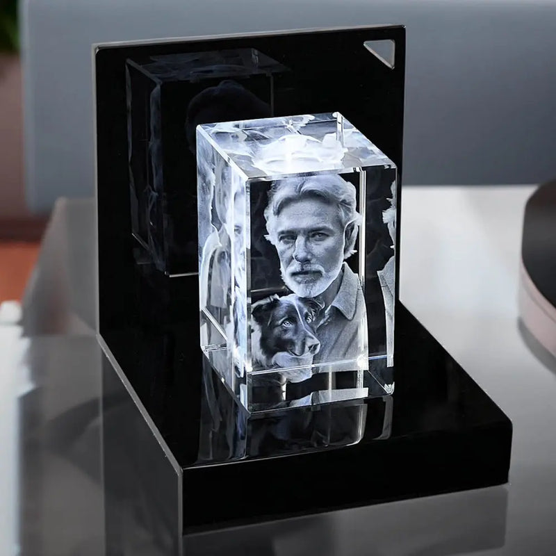 Der Engravy 3D-Glasblock Hochformat aus Kristallglas zeigt das Porträt eines Mannes und seines Hundes. Er ruht auf einem LED-Leuchtsockel, der die Gravur beleuchtet und ihre komplizierten Details mit einem faszinierenden Glanz hervorhebt.