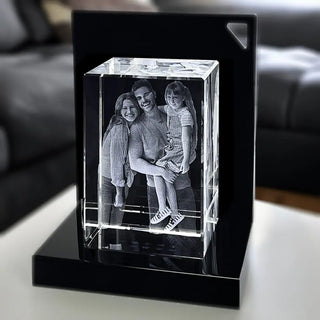 Der Engravy 3D-Glasblock Hochformat zeigt eine detaillierte 3D-Gravur einer lächelnden Familie, die in einen Kristallwürfel eingraviert ist. Er sitzt auf einem LED-Leuchtsockel vor einem verschwommenen Wohnzimmer und beleuchtet das komplizierte Design.
