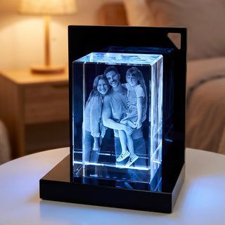 Nahaufnahme: 3D-Glasblock Hochformat mit graviertem Familienfoto, blau beleuchtet auf einem LED-Sockel im Schlafzimmer