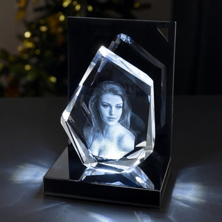 3D-Glasdiamant The Diamond mit graviertem Frauenporträt, von unten beleuchtet auf einem LED-Sockel vor unscharfen Weihnachtslichtern