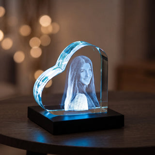 Liegendes 3D-Glasherz mit Porträtgravur einer Frau, blau beleuchtet auf dem Sockel