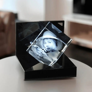 Ein Engravy 3D-Glaswürfel mit Gravur ruht elegant auf einem LED-Leuchtsockel, der auf einem runden Tisch vor einem sanft verschwommenen Wohnzimmerhintergrund angeordnet ist und so Tiefe und Faszination verleiht.
