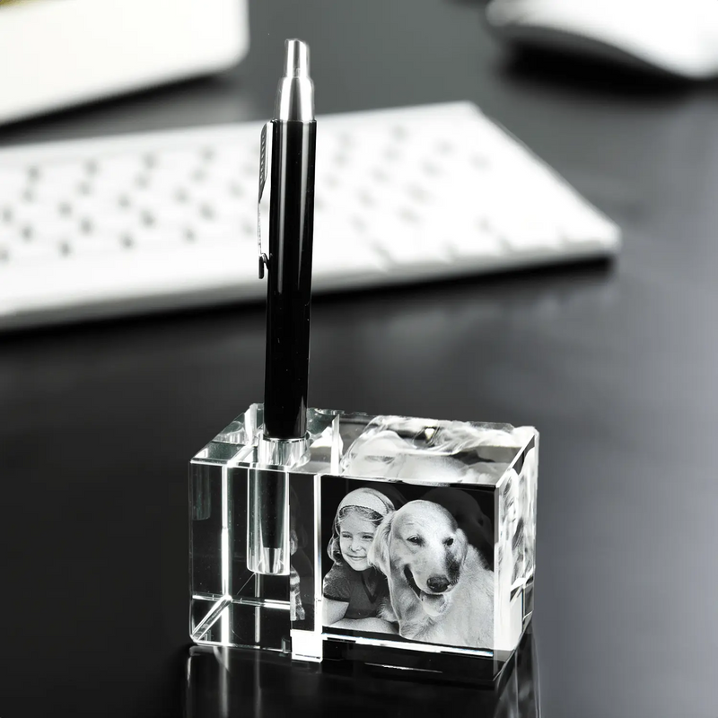 Ein Engravy 3D-Stiftehalter mit Foto-Gravur verleiht dem Schreibtisch eine persönliche Note, da er einen schwarzen Stift hält. Daneben verstärken Schwarzweißfotos von einem Kind und einem Hund den Charme, während die schwache Silhouette einer Tastatur diese gemütliche Arbeitsplatzumgebung vervollständigt.
