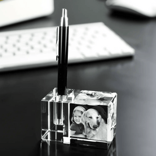 Ein Engravy 3D-Stiftehalter mit Foto-Gravur verleiht dem Schreibtisch eine persönliche Note, da er einen schwarzen Stift hält. Daneben verstärken Schwarzweißfotos von einem Kind und einem Hund den Charme, während die schwache Silhouette einer Tastatur diese gemütliche Arbeitsplatzumgebung vervollständigt.