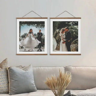 Zwei gerahmte Hochzeitsfotos hängen über einem beigen Sofa mit dekorativen Kissen. Im linken Rahmen wirbelt eine Braut in ihrem Kleid herum, und im rechten umarmt sich das Paar. Ein Bündel getrockneter Weizen ziert den Couchtisch, dezent ergänzt durch die Clipwood Wandbild-Hochformatrahmen von Engravy.