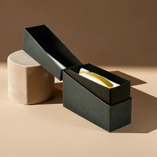 Elegante schwarze Geschenkbox mit personalisiertem Gold-Armband auf beigem Samt-Podest - luxuriöse Geschenkverpackung für gravierte Armbänder
