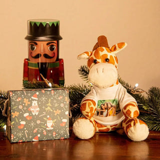 Eine Kuschelgiraffe mit Foto von Engravy, in einem weißen Hemd, sitzt neben einem verpackten Geschenk auf einem Tisch. Ein dekorativer Nussknacker und festliches Grün mit kleinen Lichtern sorgen für eine gemütliche Szene. Das Geschenkpapier mit Weihnachtsmotiv macht es perfekt als persönliches Geschenk.