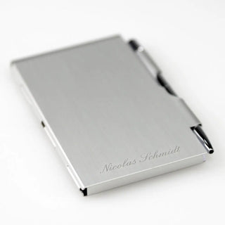 Der Notizblock mit Gravur von Engravy ist ein eleganter Visitenkartenhalter aus Aluminium mit minimalistischem Design und integriertem Stift. Er trägt den eingravierten Namen „Nicolas Schmidt“ und verleiht dem schlichten weißen Hintergrund eine elegante Note, perfekt für jeden Berufstätigen.