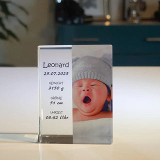 Engravys „Personalisierbares Foto in Glas – Hochformat“ zeigt elegant das Foto eines gähnenden Babys mit Angaben zu Name, Geburtsdatum, Gewicht, Länge und Uhrzeit auf der linken Seite. Das charmante Porträt ruht auf einer hellen Oberfläche.