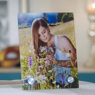 In einem Feld voller Wildblumen hält eine Frau mit langen braunen Haaren in einem weißen Tanktop Blüten. Der unscharfe Hintergrund ähnelt Engravys „Personalisierbares Glasbild mit Alufüßen – Halte deine Erinnerungen fest“ und verbindet natürliche und Innenraumästhetik nahtlos.