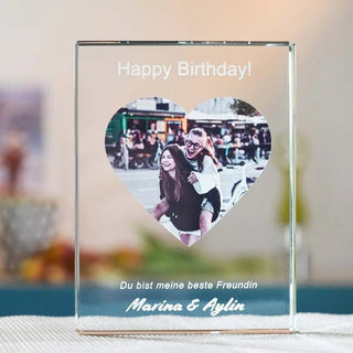 Das gravierte personalisierbare Glasfoto im Hochformat zeigt einen herzförmigen Ausschnitt mit einem fröhlichen Bild einer Person, die eine andere Huckepack mitnimmt, sowie dem Text „Happy Birthday! Du bist meine beste Freundin. Marina & Aylin.“.