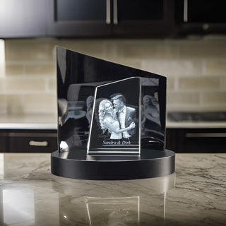 Engravys Premium 3D-Glasgravur – Der Turm zeigt ein tanzendes Paar, das elegant auf einem schwarzen runden Sockel auf einer Marmorarbeitsplatte balanciert. Im verschwommenen Küchenhintergrund steht auf der Gravur „Besonderer Moment Sandra & Dirk“, was das außergewöhnliche Design für besondere Anlässe hervorhebt.