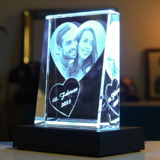 Das Engravy Selbststehende 2D-Glasbild im Hochformat zeigt ein lächelndes Paar in einem Herzen mit der Gravur „02. Februar 2023“. Das personalisierte Kunstwerk sitzt auf einem dunklen Sockel mit einem LED-Leuchtsockel, der für sanfte Beleuchtung sorgt.