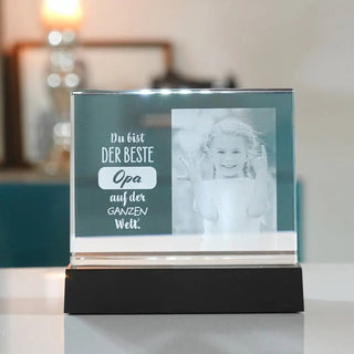 Das selbststehende 2D-Glasbild im Querformat von Engravy zeigt ein lächelndes Schwarz-Weiß-Foto eines Kindes mit dem Text „Du bist DER BESTE Opa auf der GANZEN Welt“, was bedeutet: „Du bist der beste Opa auf der ganzen Welt.“ Erwägen Sie den Einbau eines LED-Leuchtsockels für mehr Eleganz.