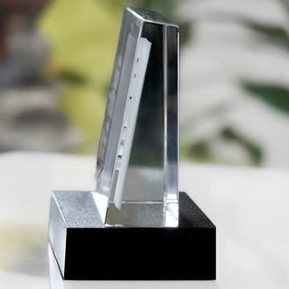 Das Engravy Selbststehende 2D Glasbild im Querformat ruht auf einer weißen Oberfläche und einem schwarzen LED-Leuchtsockel. Die leicht geneigte, rechteckige Form steht elegant vor einem unscharfen Hintergrund und kann als personalisiertes Fotogeschenk bewundert werden.