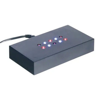 Die Engravy „Sockel Scheibe selbstehend Farbe“ ist eine schwarze rechteckige LED-Anzeige mit einem Raster aus neun Lichtern: vier rote, vier blaue und ein zentrales weißes. Mit einem seitlichen Netzkabel verstärkt sie ihre optische Wirkung auf einem Leuchtsockel perfekt.