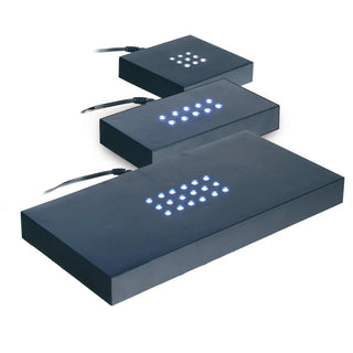 Drei schwarze rechteckige LED-Aquarienleuchten „Sockel Scheibe selbstehend Hochformat“ von Engravy sind diagonal angeordnet wie ein schlanker Glasblock. Mit blau beleuchteten Punktrastern und Kabeln von oben wird ihr modernes Design durch den schlichten weißen Hintergrund hervorgehoben.